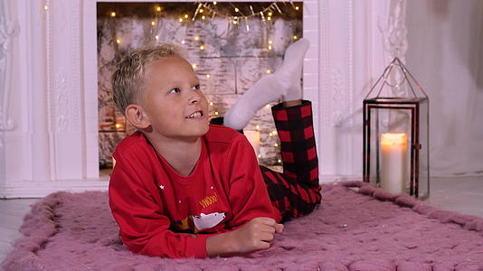 金发男孩躺在浴缸里的壁炉背景室的圣诞地板上视频的预览图
