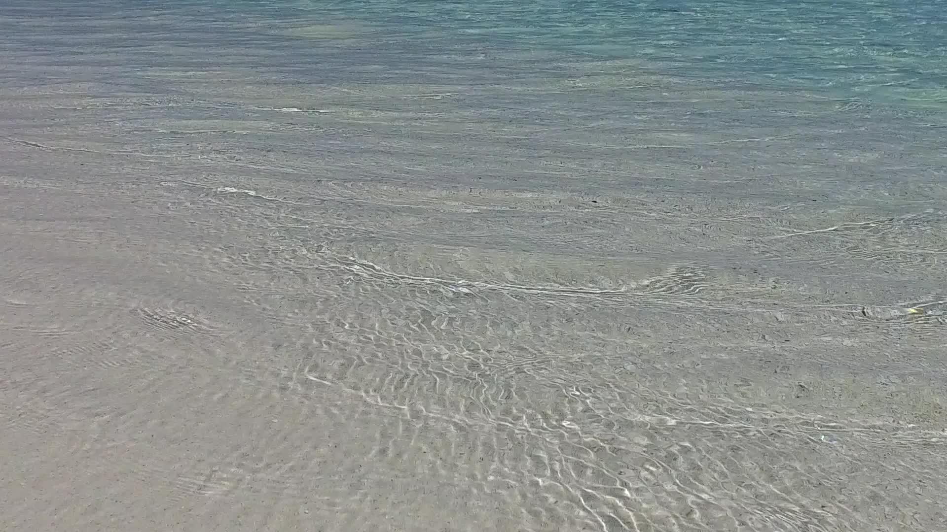 阳光明媚、宁静的海岸海滩旅游沿着浅海和接近冲浪的白沙背景视频的预览图