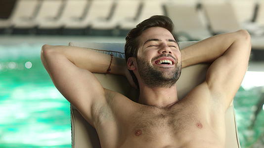 在豪华水疗中心的游泳池边放松的男人睡在休息室的池边视频的预览图