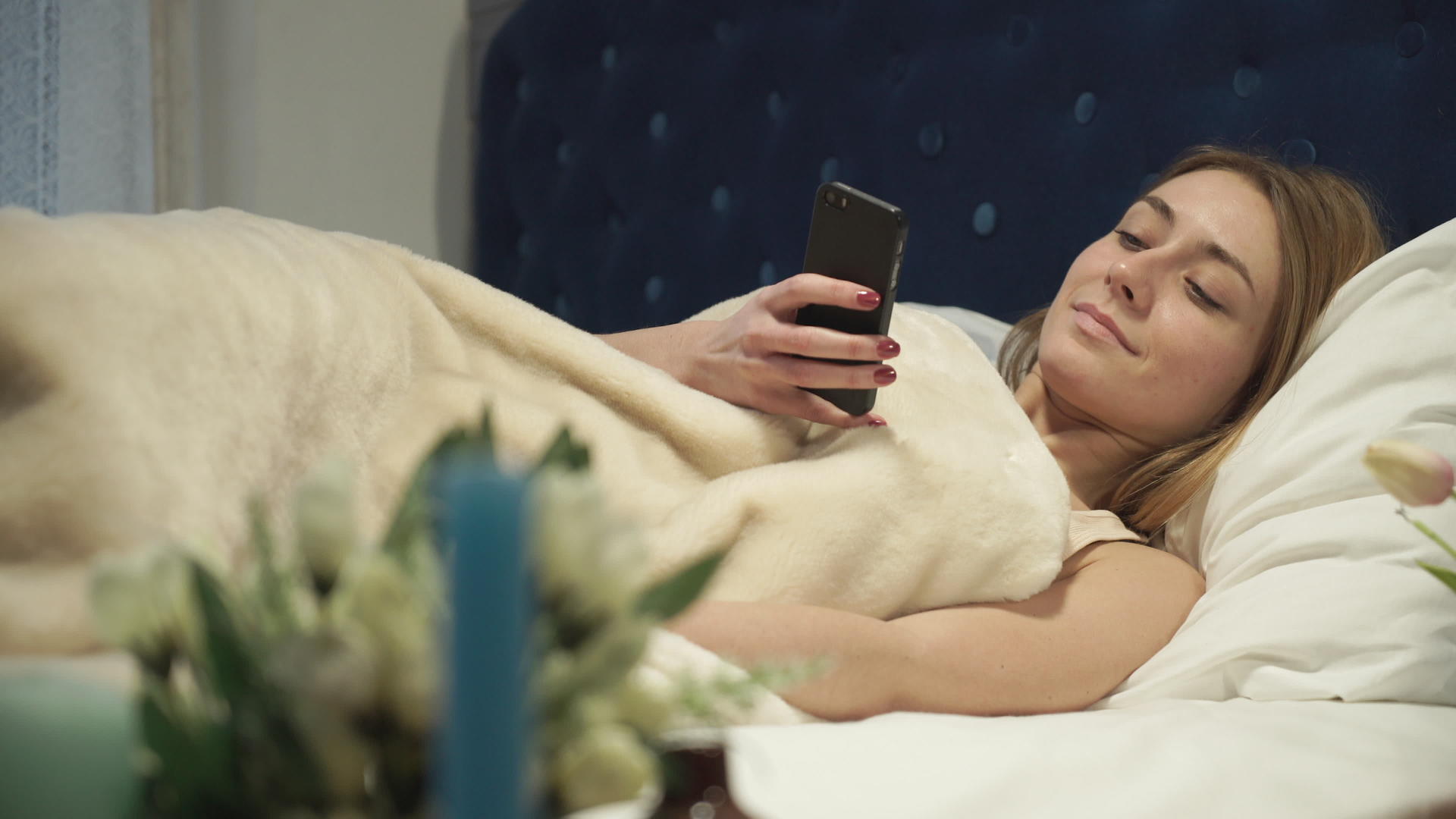 躺在床上的金发女郎在你的手机上打字视频的预览图
