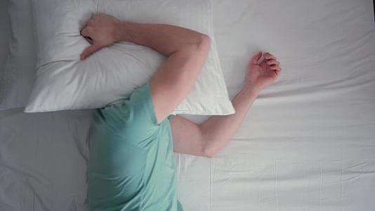 年轻人睡在床上他在睡眠中受到干扰用枕头盖住自己视频的预览图