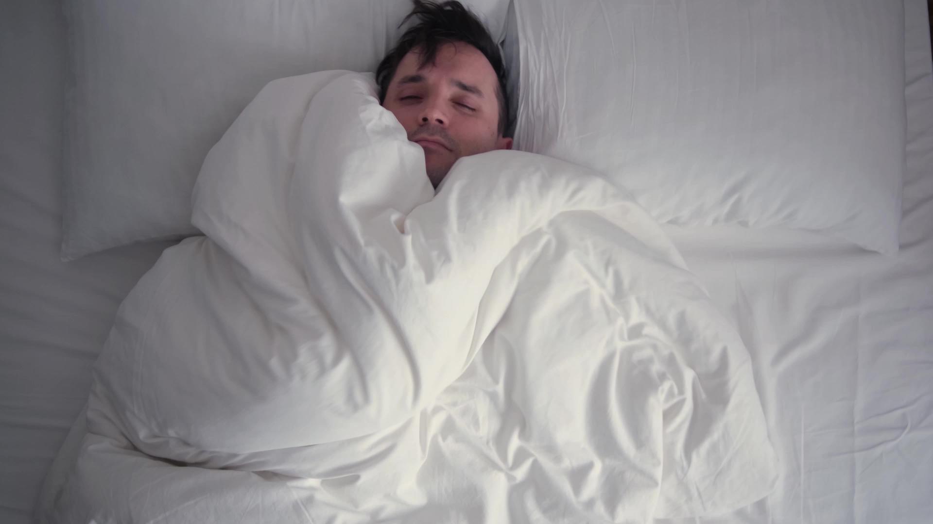 年轻人用厚厚的毯子裹着头睡得很熟冬天热白床上用品视频的预览图