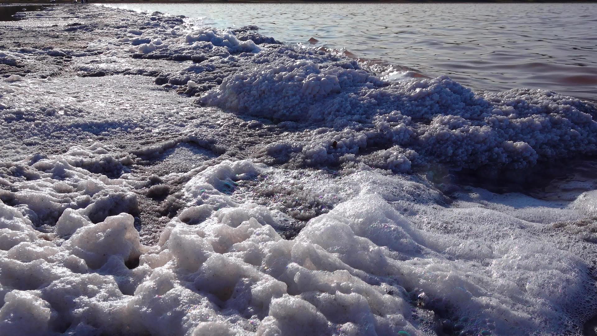盐湖岸上的石头上覆盖着白色泡沫和盐水晶体包括盐湖边的石头视频的预览图