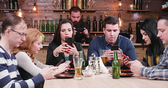 酒吧里的朋友看他们的智能手机看现代社会的问题视频的预览图