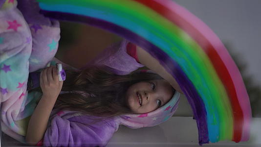穿着睡衣的女学生在家里的窗户上画彩虹视频的预览图