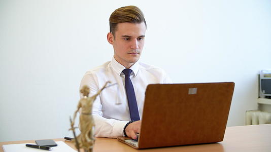 英俊的年轻律师在书桌上用笔记本电脑工作视频的预览图