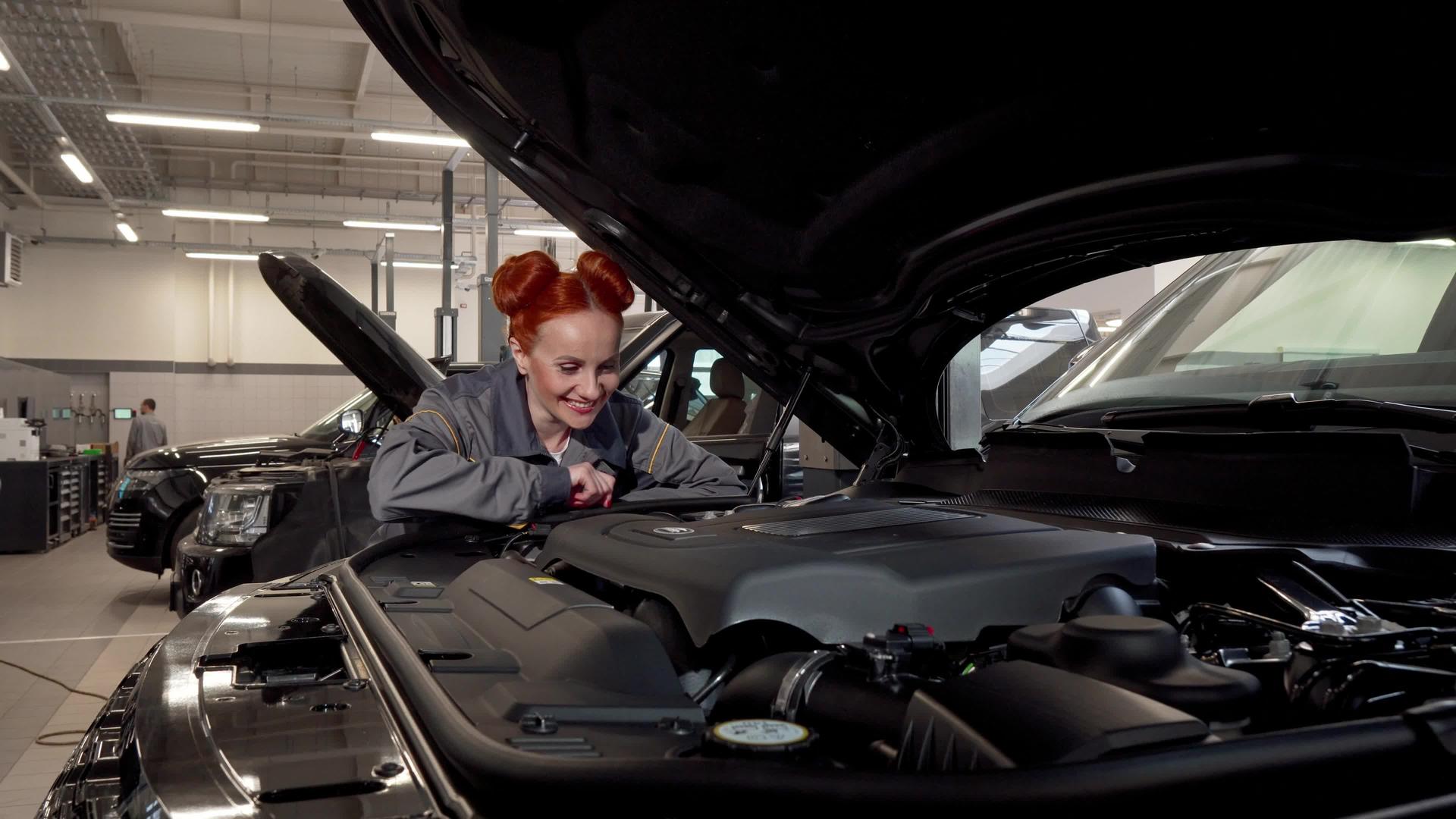 迷人的女性汽车修理工对着镜头微笑在车库里工作视频的预览图