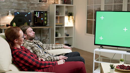一对河马夫妇坐在沙发上在电视机前用绿屏看电视视频的预览图