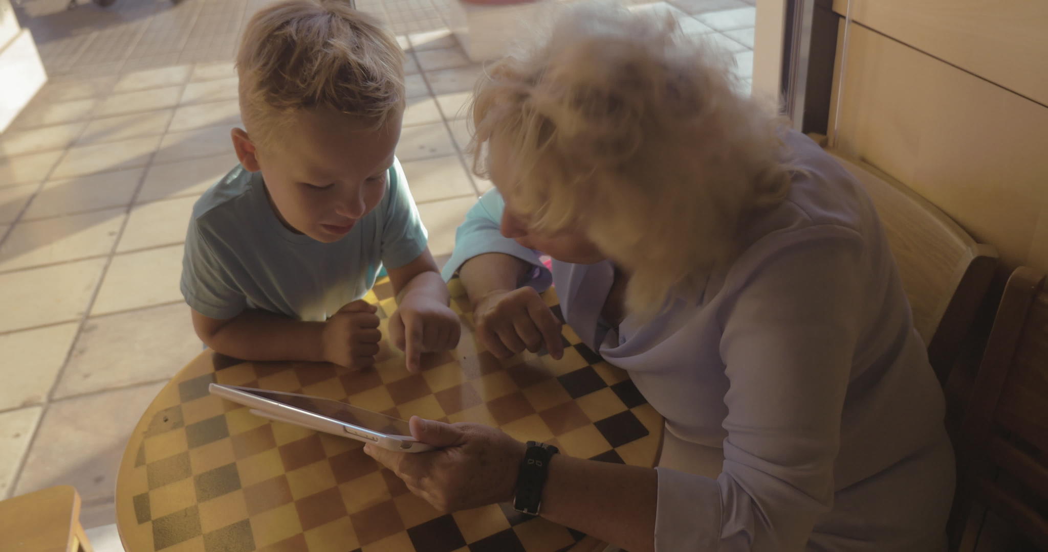 男孩和祖母在咖啡馆用触摸垫娱乐视频的预览图