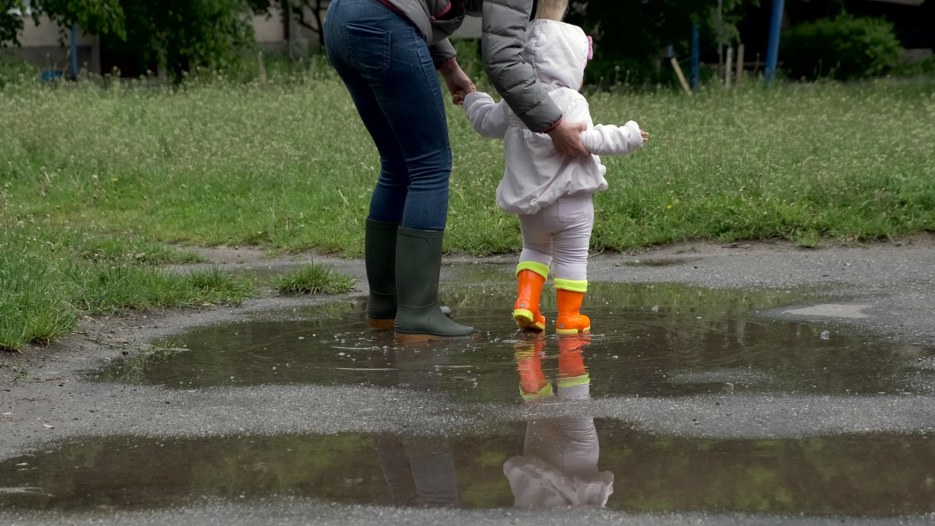 一个穿着橙色橡皮靴的小女孩和她的母亲穿过水坑视频的预览图