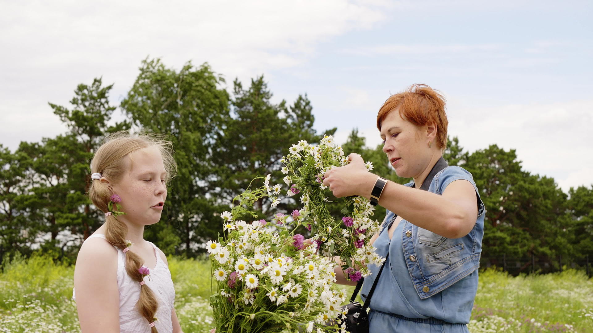 母亲和女儿在绿色的夏日田野里带着花圈和花束视频的预览图