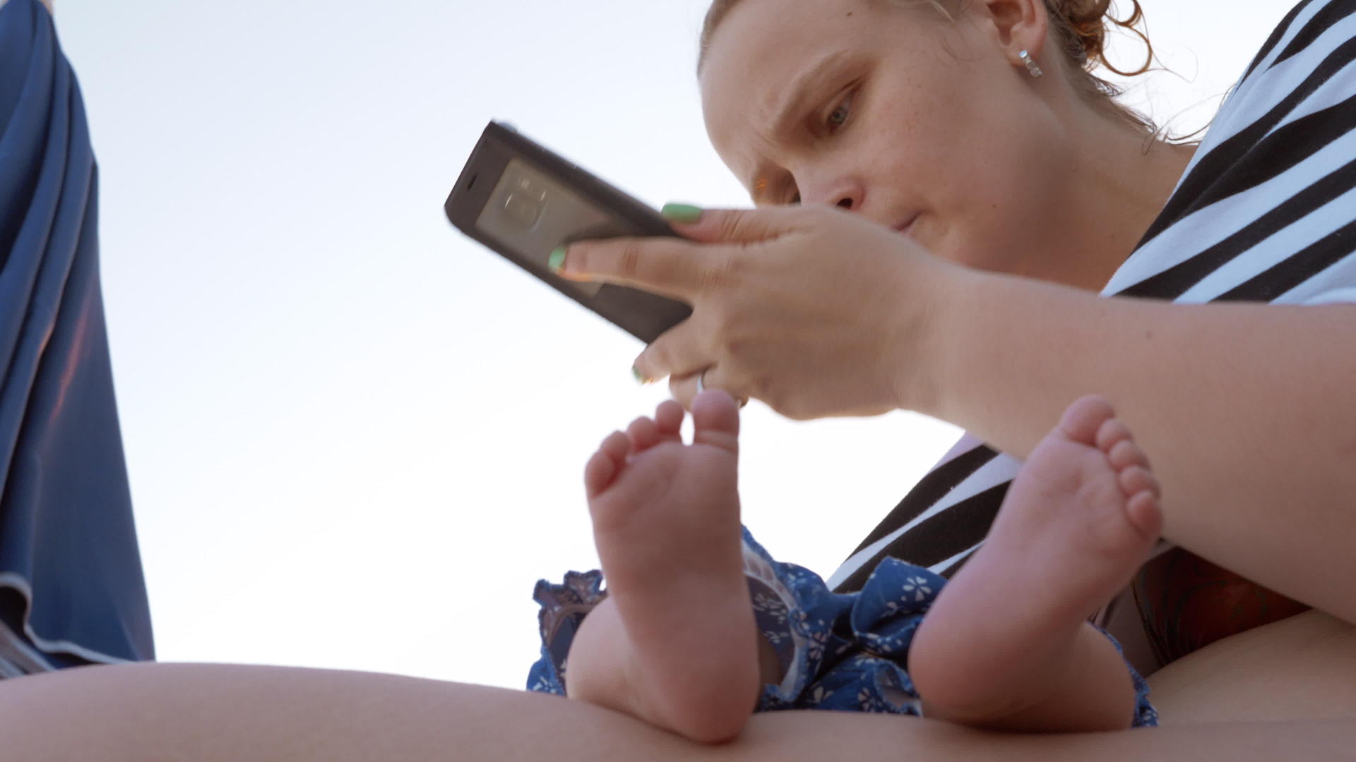母亲和熟睡的婴儿妈妈在海滩上使用手机视频的预览图