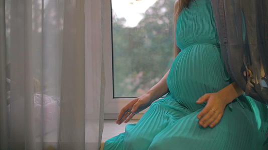怀孕的女人坐在窗台上拥抱她的肚子视频的预览图