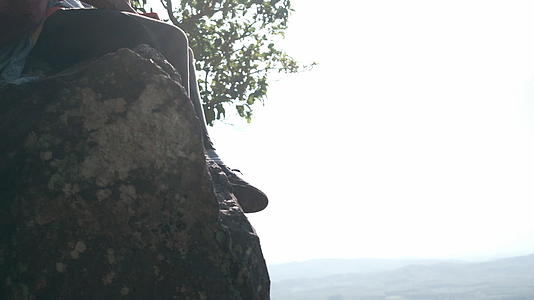泰国语是坐在悬崖上玩智能手机的年轻女性登山者衬衫上的泰国语视频的预览图
