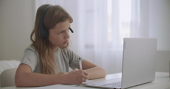 小女孩通过在网上听耳机和看笔记本来学习视频的预览图
