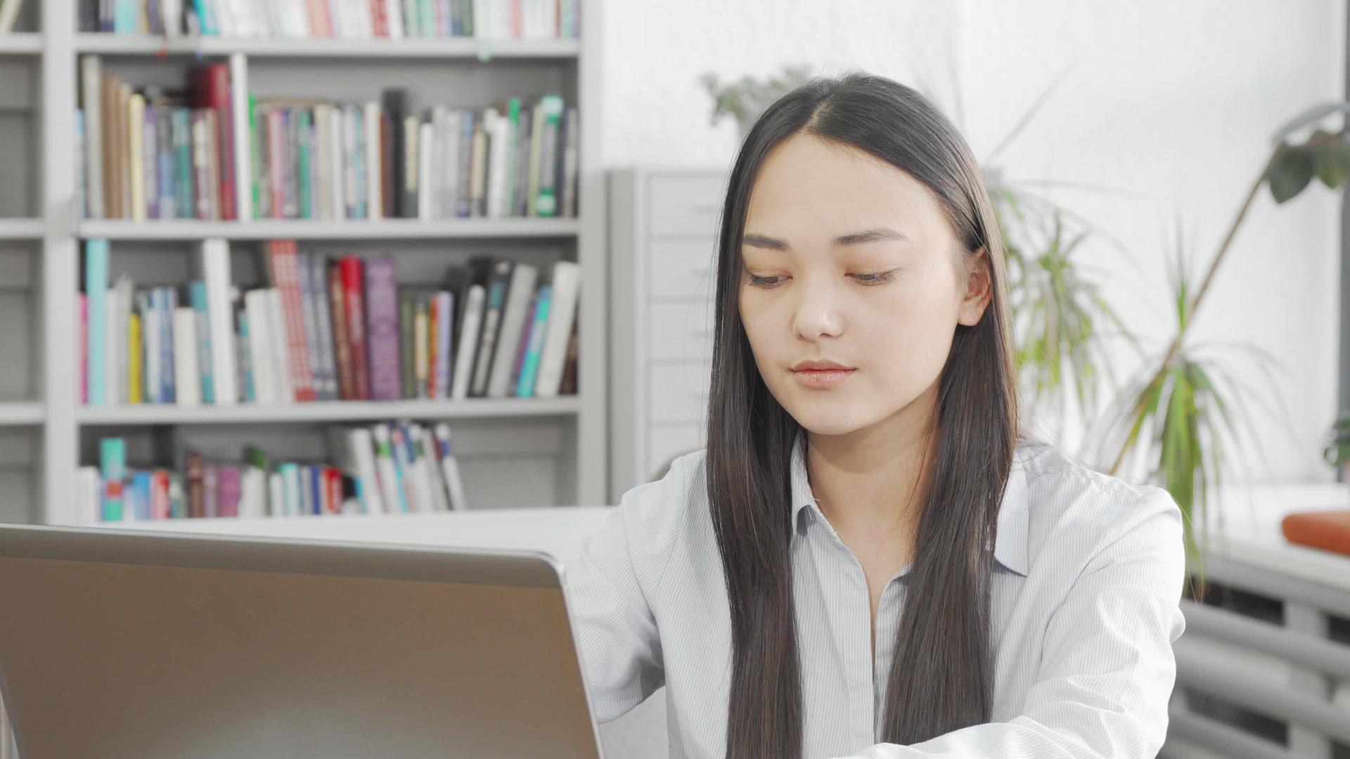 年轻的亚洲女性在图书馆使用笔记本电脑时会在相机上微笑视频的预览图