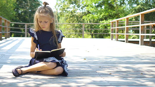可爱的小女孩在户外带着笔记和铅笔回到学校视频的预览图