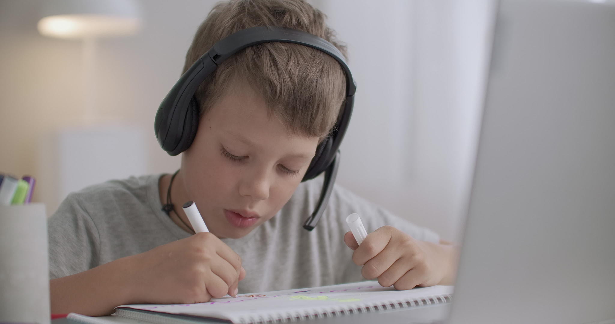 男孩在远程学习课上用耳机听老师讲耳机并在复印本上画画视频的预览图