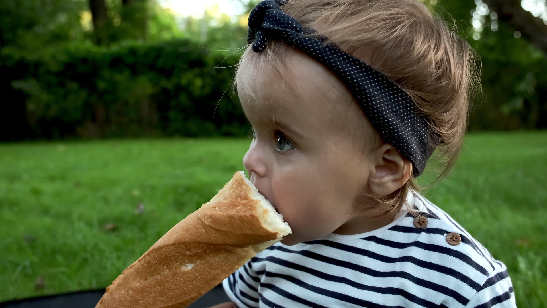 一个可爱的小女孩拿着新鲜的面包坐在花园的草坪上视频的预览图