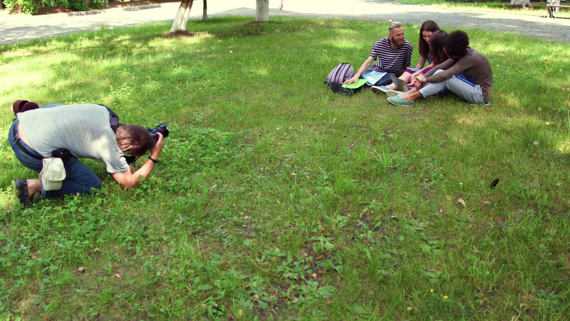 摄影师拍摄学生坐在草地上的照片视频的预览图