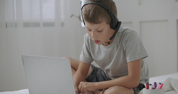 和平的学校男孩独自在房间里画画用笔记本电脑看耳机视频的预览图