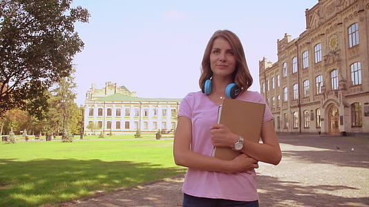 快乐的女人带着笔记本在校园地区行走视频的预览图