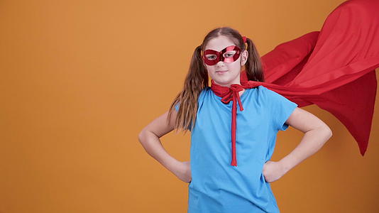 可爱的年轻女孩在橙色背景下扮演超级英雄视频的预览图