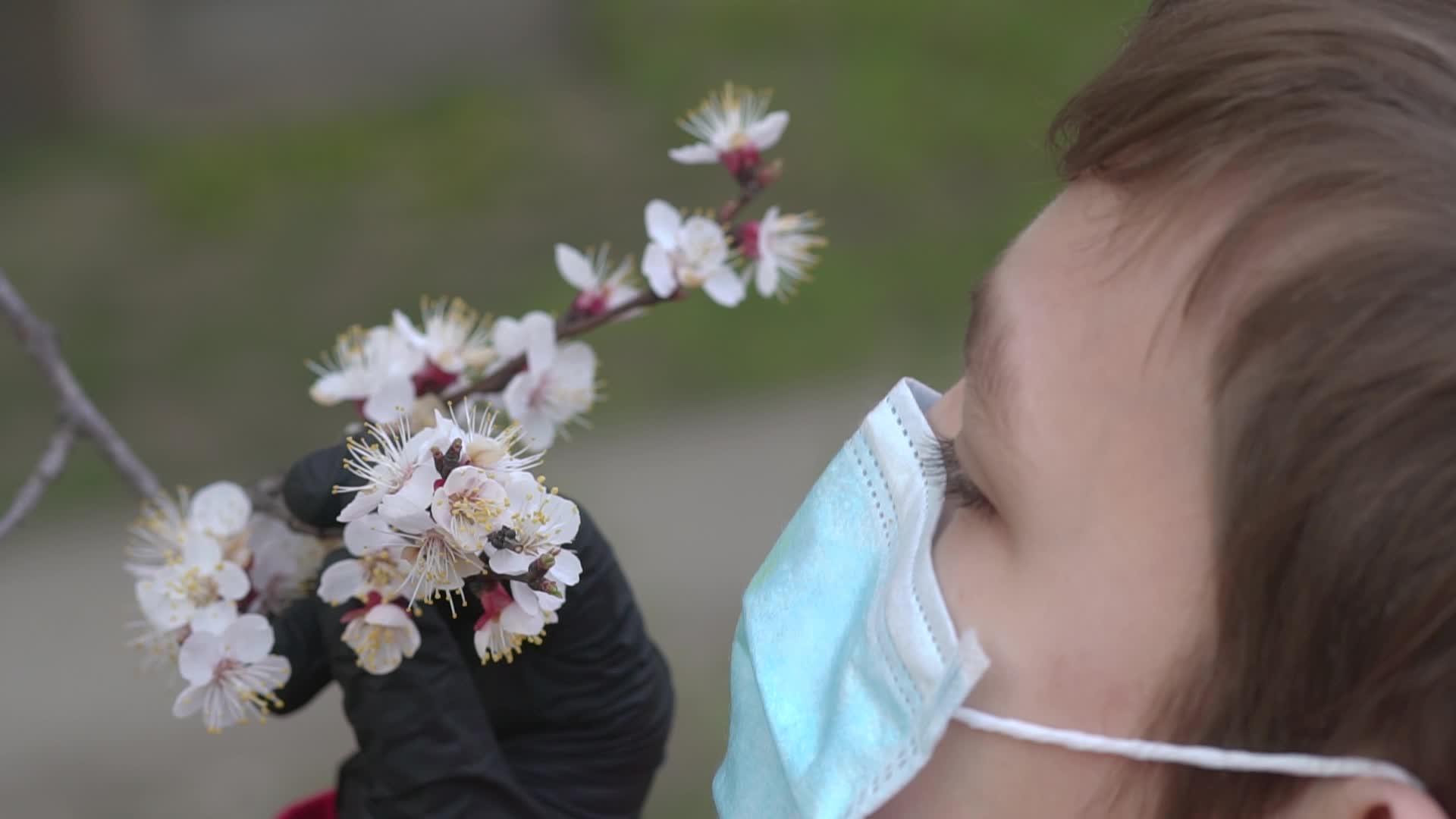 一个戴着防护医用口罩的孩子正在采取防止嗅花的保护措施视频的预览图