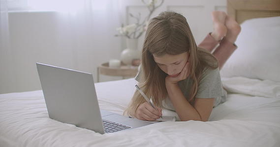 这个无聊的小女孩正在抄本做作业上网看笔记本电脑视频的预览图