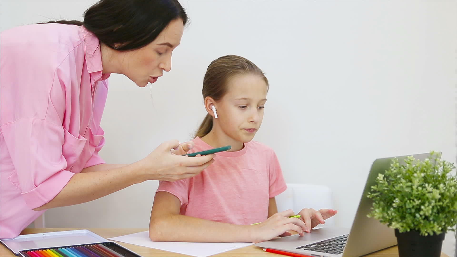女孩坐在桌子上拿着笔记本和教科书做作业同时她年轻的母亲帮助她视频的预览图