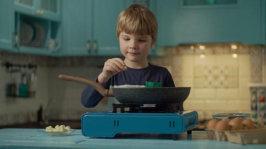 年轻的学龄前男孩独自站在家里的蓝色厨房里煮鸡蛋视频的预览图