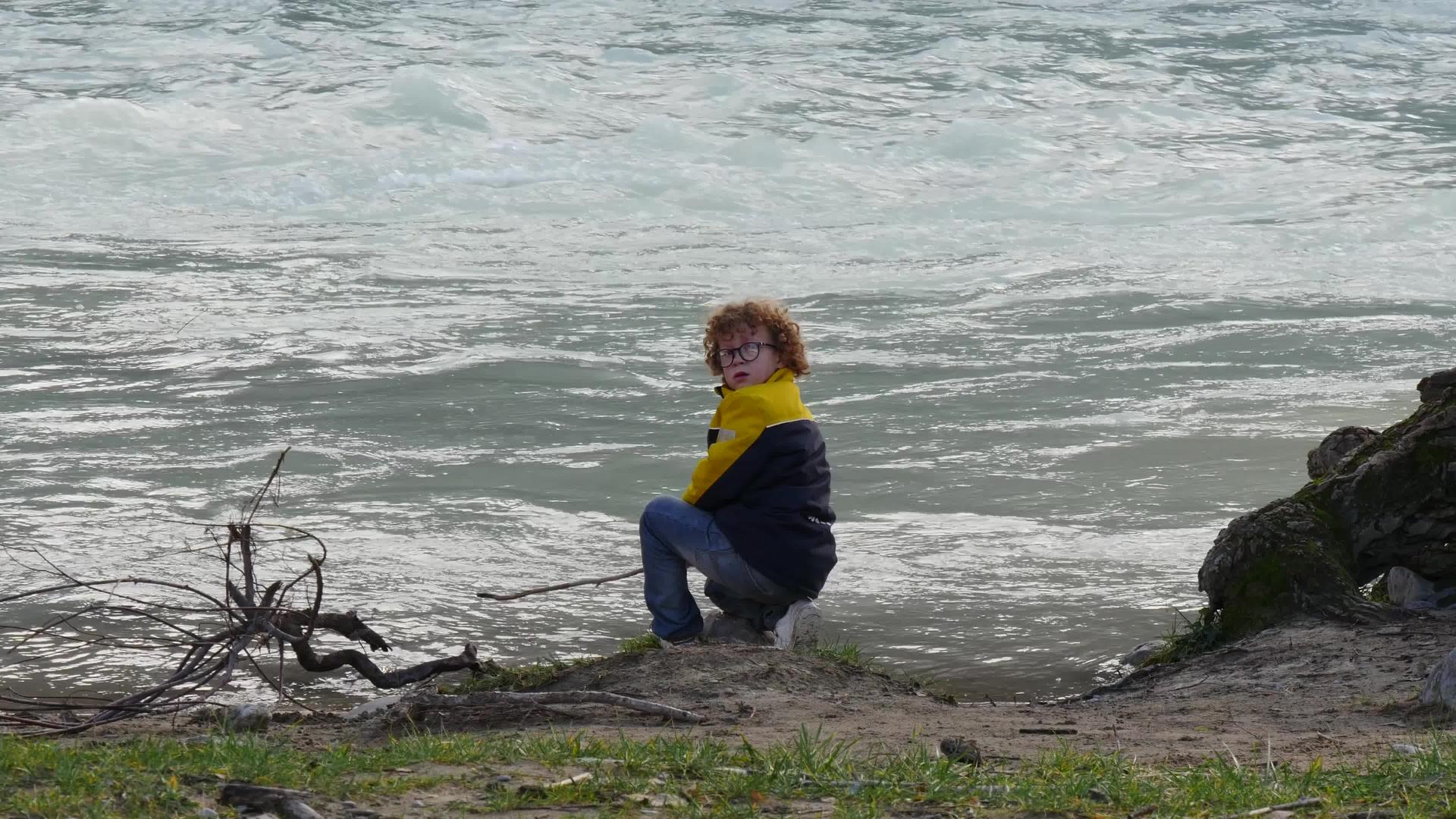 秋天在河边玩耍的卷发男孩视频的预览图