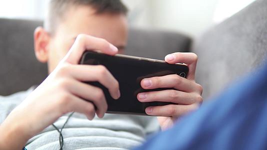 男孩用智能手机坐在沙发上男孩独自在家玩手机游戏视频的预览图