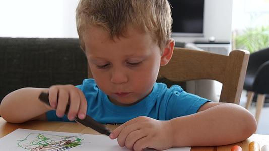 一个可爱的小男孩用彩色铅笔在纸上画画视频的预览图