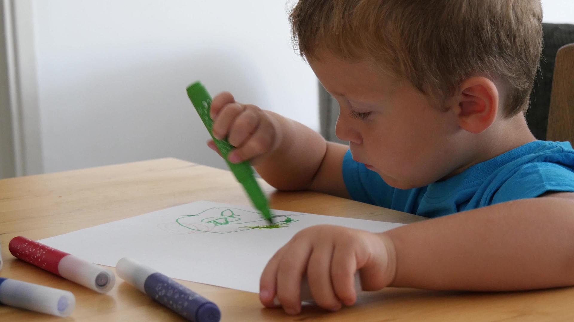 一个可爱的小男孩用彩色铅笔在纸上画画视频的预览图