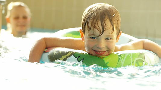 快乐的小男孩在游泳池里用橡皮环游泳视频的预览图
