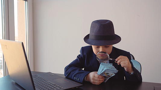 这个男孩看起来像一个商人在检查帽子和西装中的美元和放大镜视频的预览图