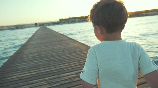小男孩日落时在码头上跑视频的预览图