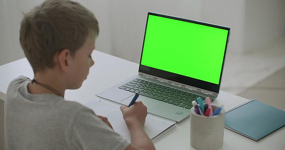 小男孩正坐在桌子旁边画画笔记本电脑上有一个关键色度技术的绿色屏幕视频的预览图