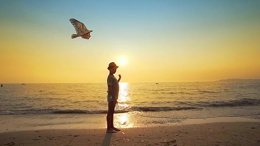 男孩的休眠钟戴着帽子在开阔的海滩上放风筝在夏天日落视频的预览图
