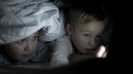 两个男孩晚上躺在床上看电影视频的预览图