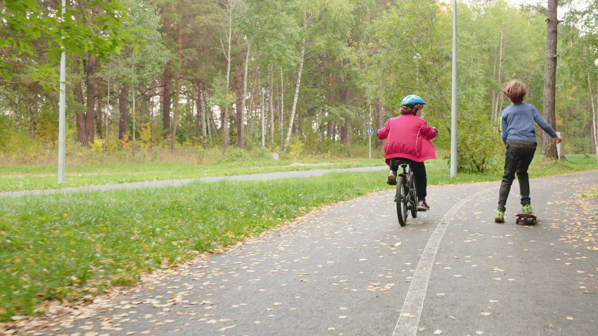 秋天公园骑自行车和滑板的年轻男孩背面的场景视频的预览图