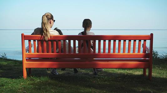坐在蓝海的草滩上坐在红色的长凳上完美地看着海边的风景视频的预览图