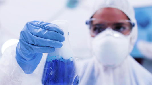 女科学家在保护设备上靠近女科学家她拿着一瓶含烟蓝色的液体视频的预览图