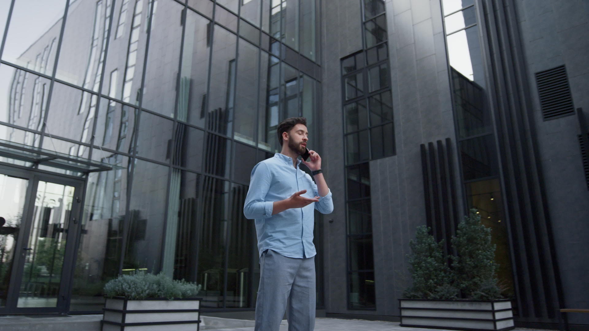在现代玻璃建筑中有魅力的男人打电话视频的预览图