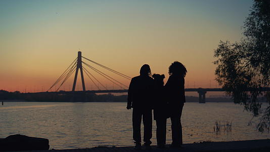 父母和孩子一起站在河桥景观中看日落的剪影视频的预览图