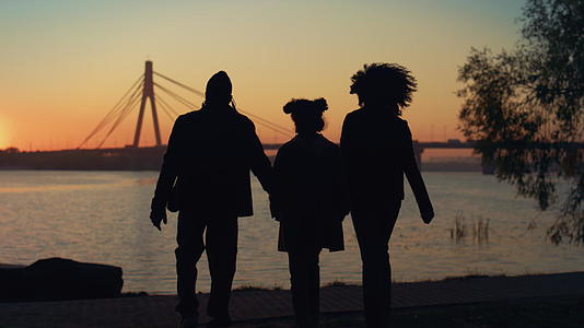 一起走到河岸在美丽的夕阳下相爱的家庭剪影视频的预览图