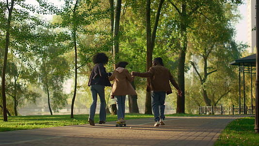 在阳光明媚的秋天公园镜子里女孩骑着长板牵着父母的手视频的预览图