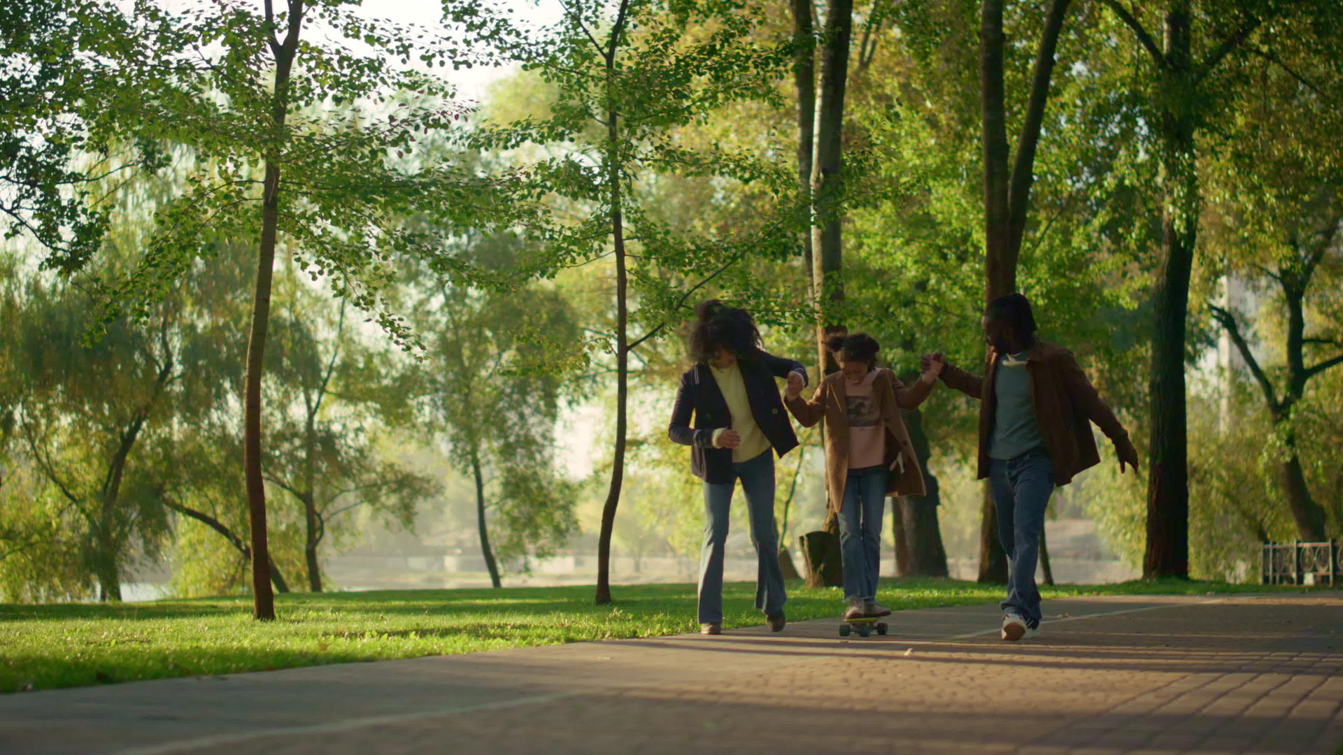 父母在阳光明媚的绿色公园里抱着孩子玩滑板视频的预览图