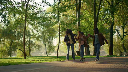 父母在阳光明媚的绿色公园里抱着孩子玩滑板视频的预览图